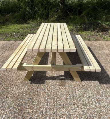 Wooden picnic table with attached benches, set on a gravel surface surrounded by grass.